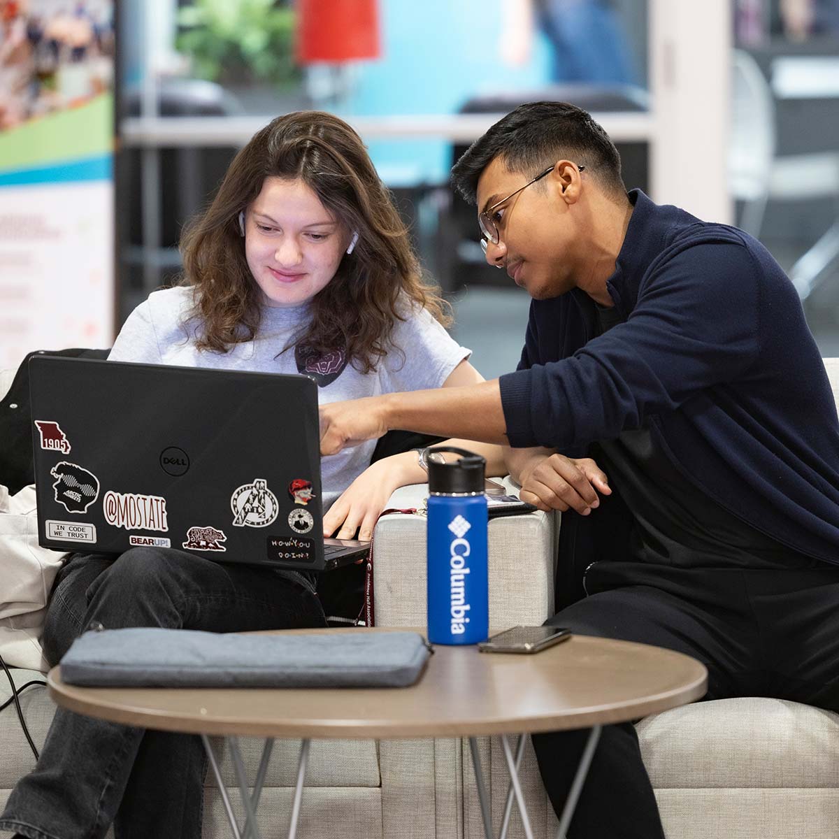 Two students looking at code on a laptop in a study lounge.