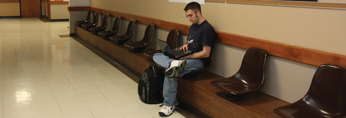 A student uses a laptop while waiting in the hallway