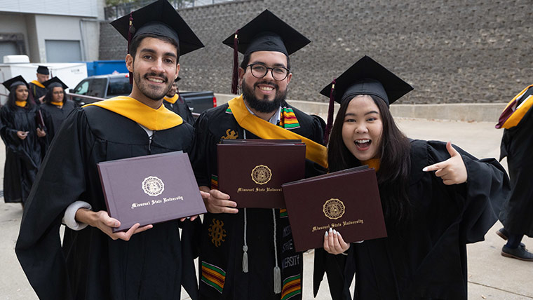 Three Missouri State students smiling while holding up their diploma covers after commencement.