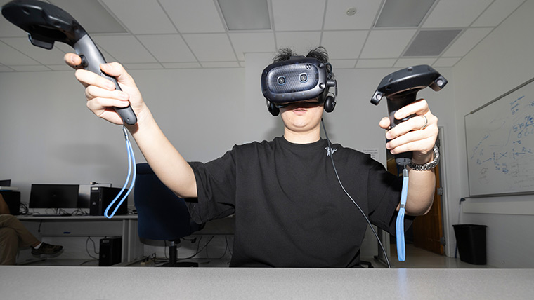 A student uses virtual reality goggles and controllers in a computer science lab.