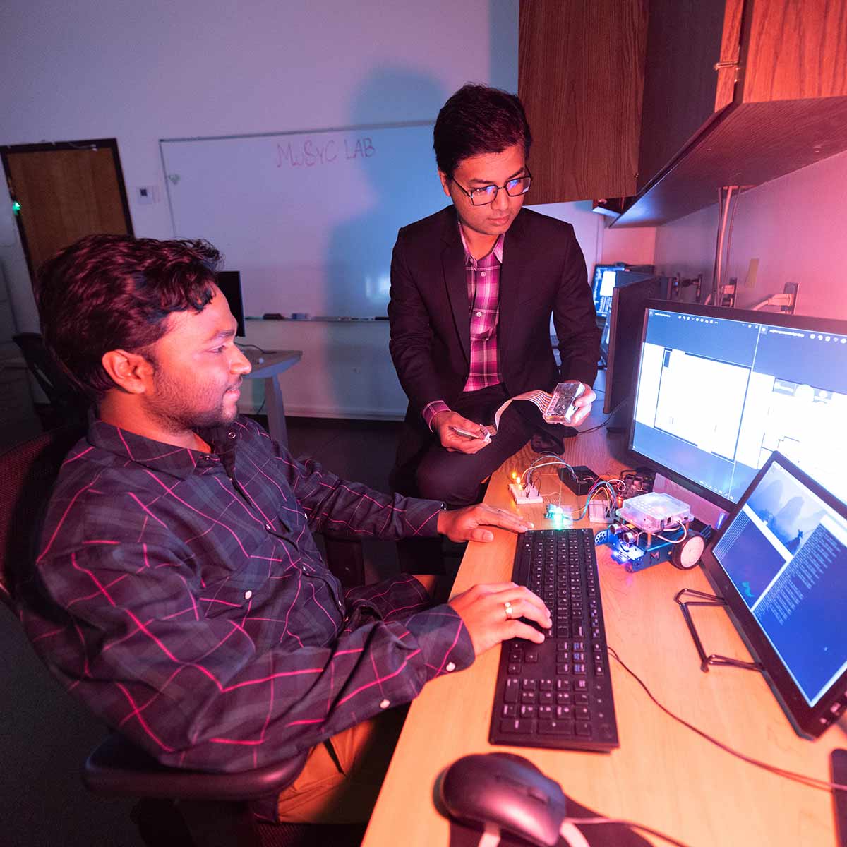 A computer science student and professor doing a demo with robotic hardware in a research lab on campus.