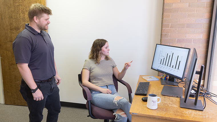 A professor and student looking at bar charts on a computer screen.