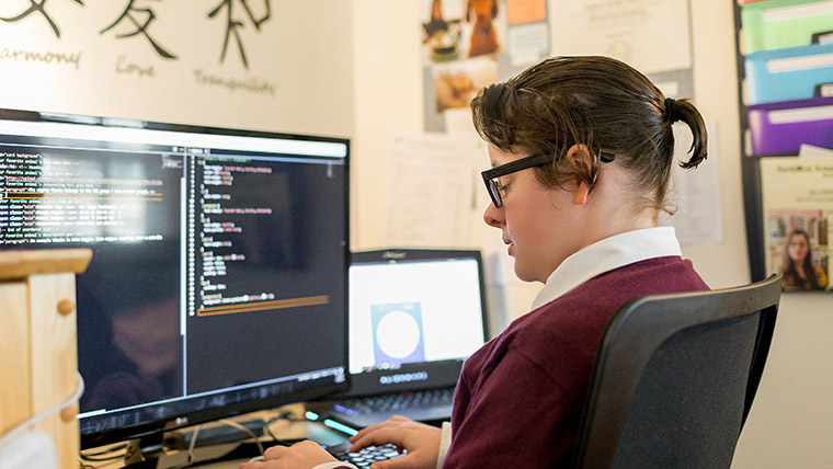 A person writes code at the computer station in their home office.