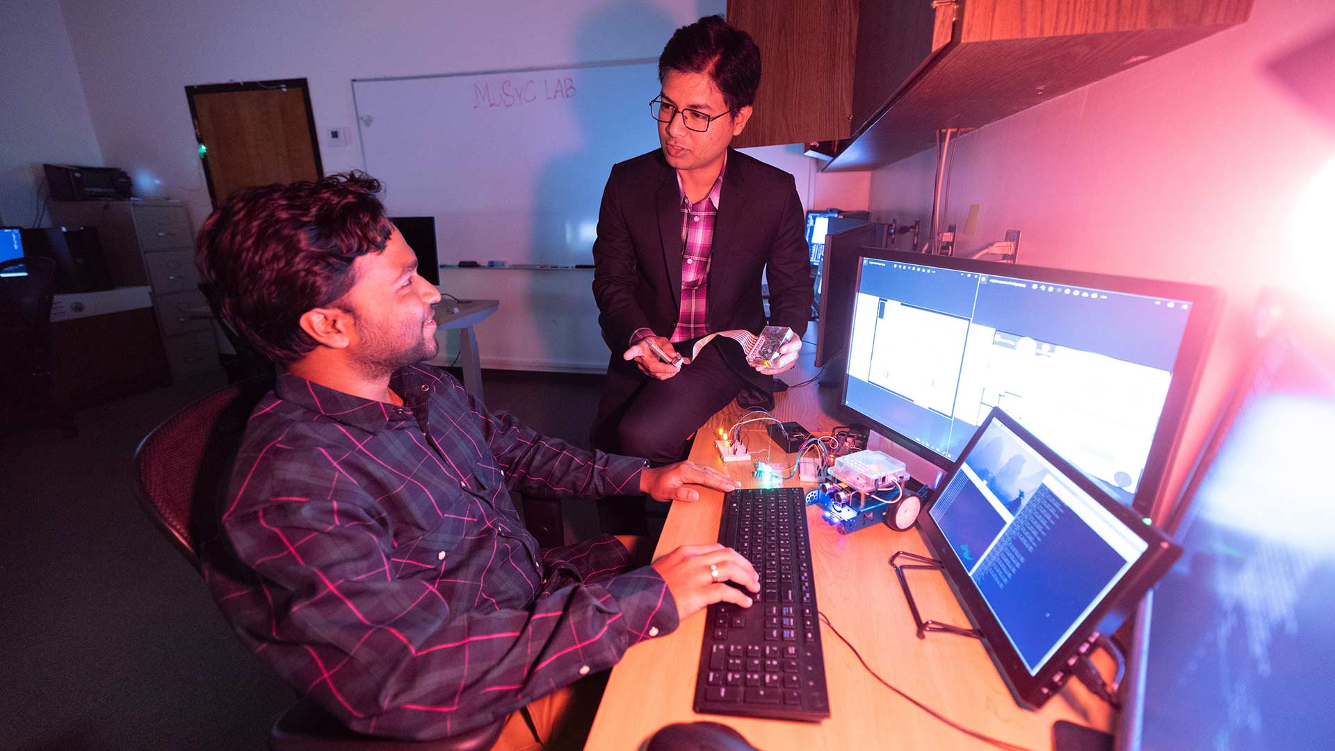 A professor and student conduct a demo on a piece of equipment in a computer science lab.