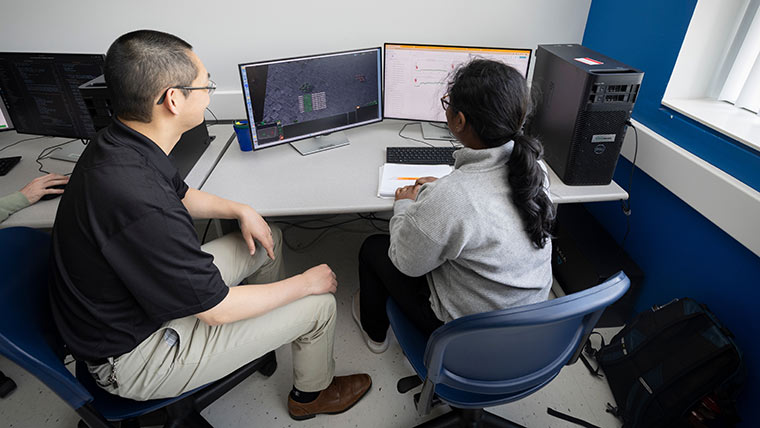 A computer science professor and student work together on a computer program in a research lab on campus.